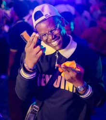 A guest in a varsity jacket grinning, phone in hand.