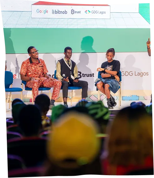 Three panellists on stage in front of the sponsor banner, with the audience in the foreground.