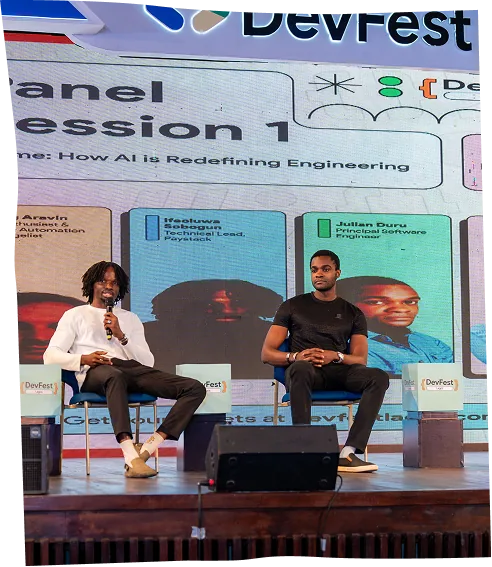 Two speakers on stage for Panel Session 1, one of them holding a microphone.
