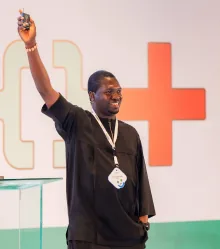 A speaker with one arm raised, smiling, in front of the DevFest stage graphics.